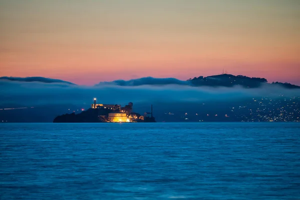 Ilha de Alcatraz ao pôr-do-sol rodeada de nevoeiro e montanhas — Fotografia de Stock