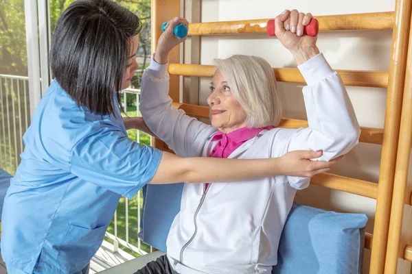 亚洲女护士一边和成熟的老年妇女一起玩耍 一边笑着 同时在有体重的戒毒所进行体育锻炼 退休社区概念 — 图库照片