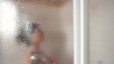 Cam kapının arkasında yıkanan bir kadının görüntüsü.