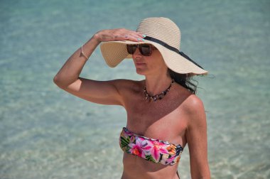 Okyanus sınırında hasır şapka takan bir kadın kafasına dokunuyor. Touri.