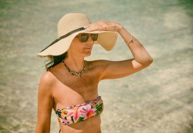 Okyanus sınırında hasır şapka takan bir kadın kafasına dokunuyor. Touri.