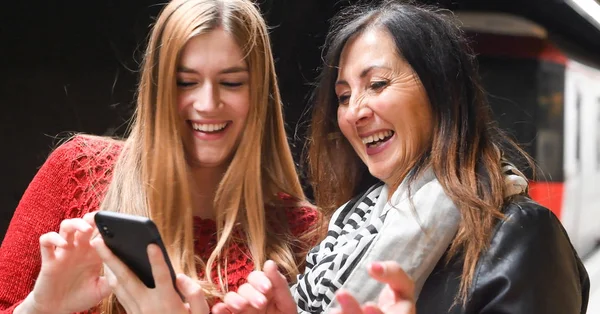 Un par de amigas sonriendo felices mirando al smartphone — Foto de Stock