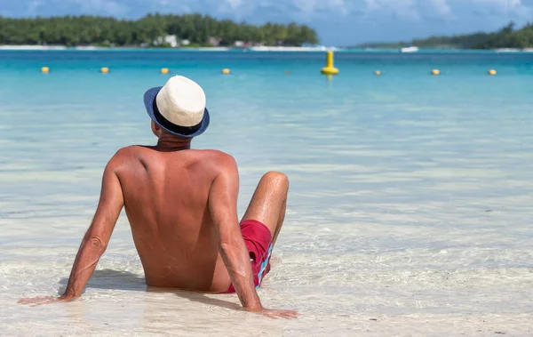 Hombre con sombrero de paja relajándose en el borde del agua en una hermosa playa —  Fotos de Stock