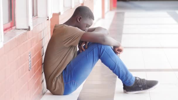 いじめられたアフリカ系アメリカ人の少年が高校のホールの床に座り — ストック動画