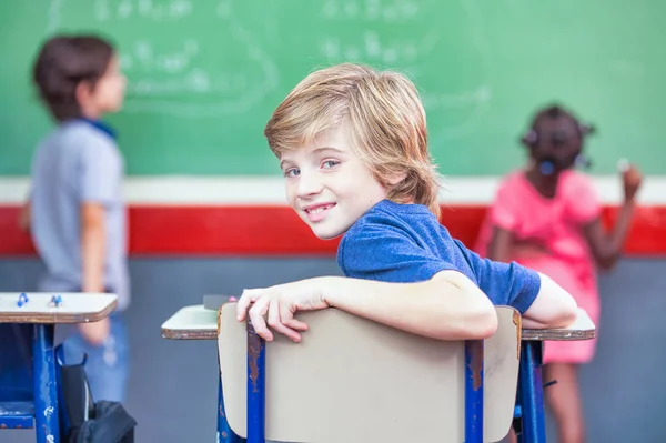 Primary school classroom. Young boy turning back to his classmat — Stock Photo, Image