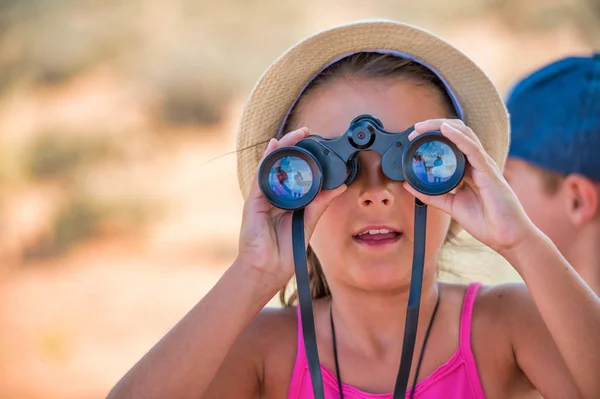 Cheerful young girl using binoculars outdoor in a park on a hot — Stock Photo, Image