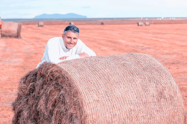 Happy man leaning on a round hay bale in the countryside — Stock Photo, Image