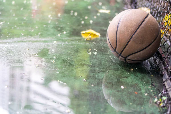 Verlaten basketbal op een buiten veld met regen en plassen — Stockfoto