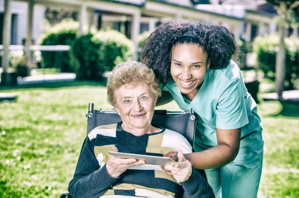 Vrouwelijke Arts Helpt Oudere Gepensioneerden Met Tablet Ziekenhuistuin — Stockfoto