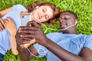 Afrikalı erkek ve beyaz kız bahçede müzik duyuyorlar..