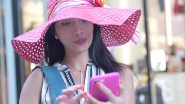 Pembe şapkalı Asyalı kız cep telefonuna mesaj yazıyor.