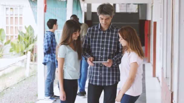 Učitel ve škole na chodbě mluví se svými studenty, kteří drží kus papíru. Zpomalený pohyb — Stock video