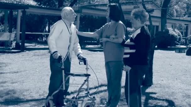 Pareja mayor leyendo periódico en el jardín asistida por una joven enfermera. Sepia tonificada — Vídeo de stock