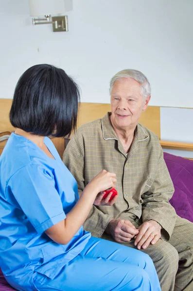 Asian nurse assisting elderly man on the hospital bed.