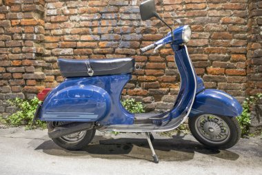 Arkasında tuğla duvar olan klasik mavi İtalyan motosikleti..