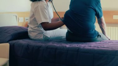 Afrikalı kadın doktor yaşlı adamı hastanede ziyaret ediyor. Steteskop kullanan kadın.