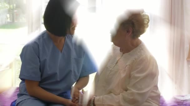 Asiatische Ärztin beruhigt ältere Frau. Beide Frauen reden auf dem Krankenhausbett — Stockvideo