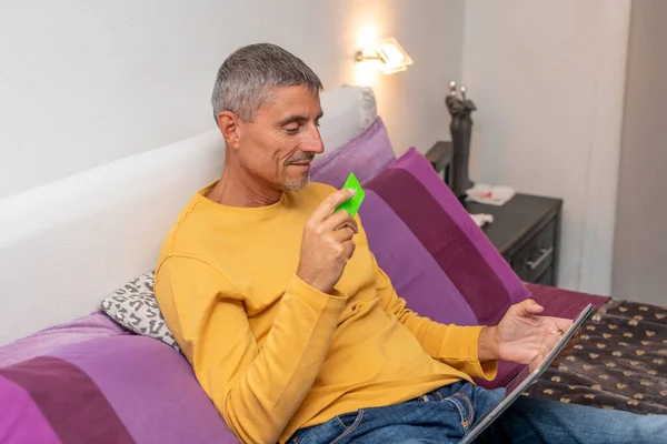 快乐的高加索男人在沙发上用平板电脑和信用卡购物 — 图库照片
