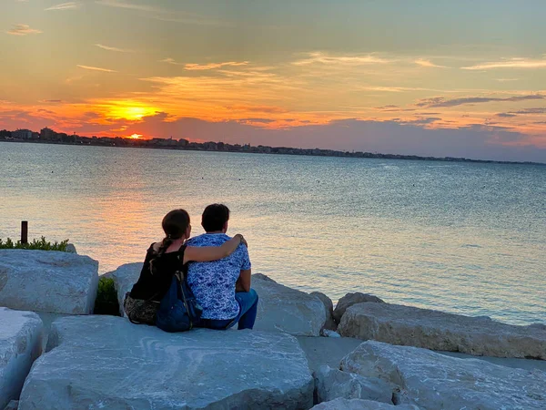 Güzel bir sahil boyunca gün batımını izleyen genç bir çift..