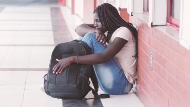 Грустный африканский подросток, сидящий в школьном коридоре и думающий о своих проблемах — стоковое видео