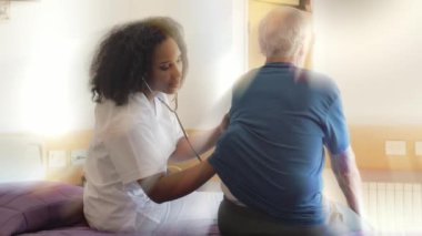 Steteskoplu genç Afrikalı doktor hastane odasında yaşlı bir adamı ziyaret ediyor. Arkadan gelen ışık ışınları