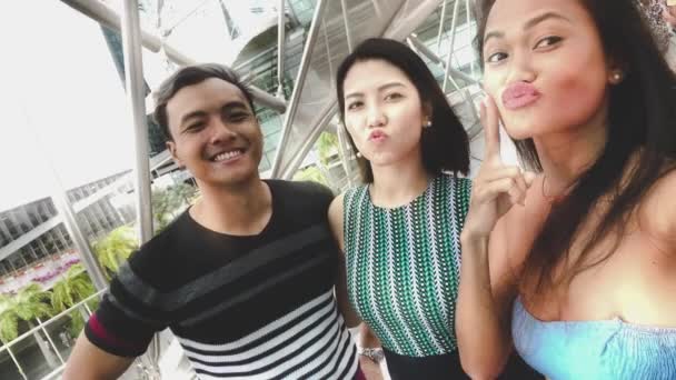 Three asian friends enjoying outdoor city life, taking selfies and making grimaces to the camera. Friendship and holiday concept — Stock Video