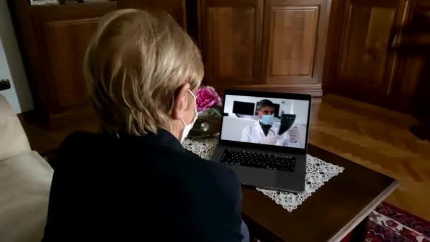 Ältere Frau zu Hause webt Maske in Coronavirus-Zeiten auf einem Videotelefon mit ihrem Arzt — Stockvideo