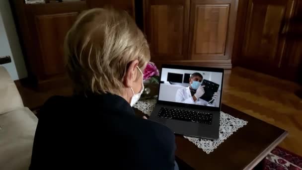 Ältere Frau zu Hause webt Maske in Coronavirus-Zeiten auf einem Videotelefon mit ihrem Arzt — Stockvideo