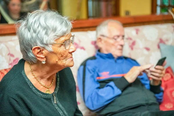 自宅のソファの上で高齢者の成熟したカップル 女の話スマートフォンを使う男 — ストック写真