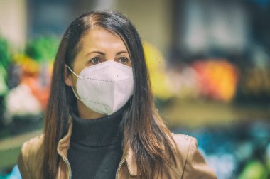 Süpermarkette yüz maskesi takan beyaz bir kadın. Coronavirüs krizi sırasında ya da covid19 salgını sırasında raftan alışveriş malzemesi almak isteyen bir kız..