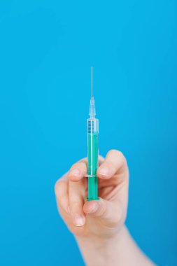 Mavi arka planda şırıngayı tutan kadın doktor.