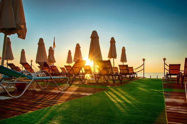 chaise lounges with umbrellas on wooden pier in Turkey hotel at sunrise