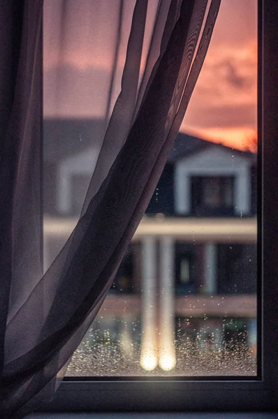 indoor view of  window glass with raindrops and blurred house outside