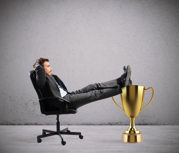 Переможець бізнесмен розслабляється над золотою чашкою — стокове фото