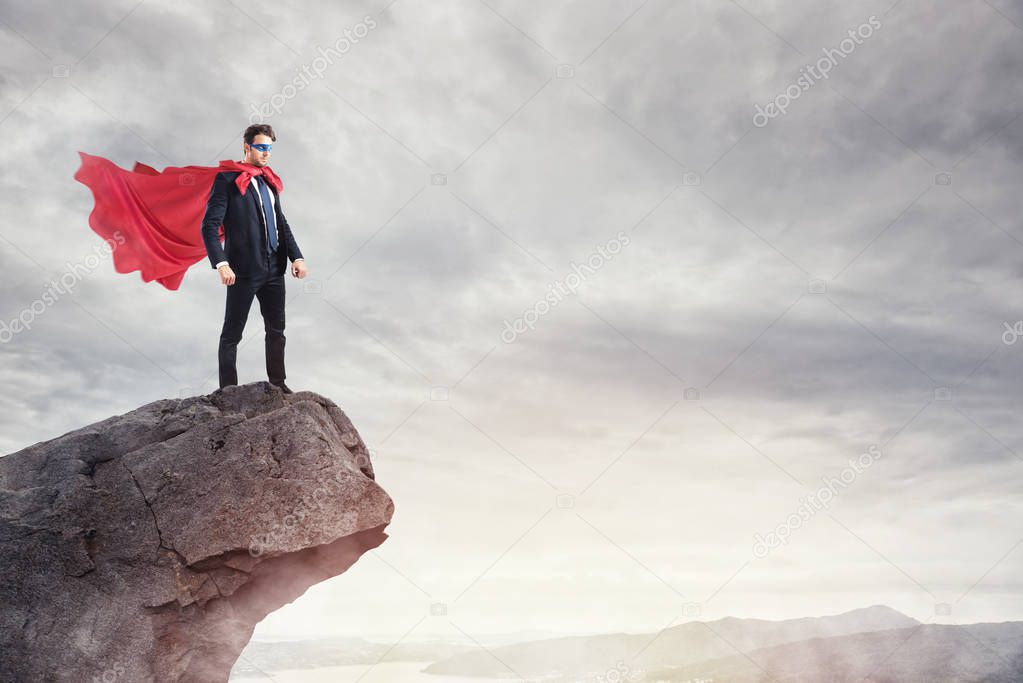 Businessman as a super hero on the peak of a mountain