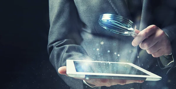 Businessman examines a tablet with a magnifying glass. Concept of internet security — Stock Photo, Image