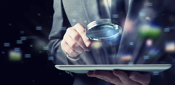 Businessman examines a tablet with a magnifying glass. Concept of internet security — Stock Photo, Image