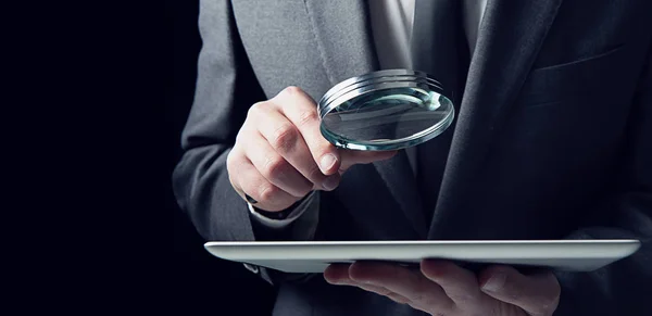 Businessman examines a tablet with a magnifying glass. Concept of internet security — Stock Photo, Image