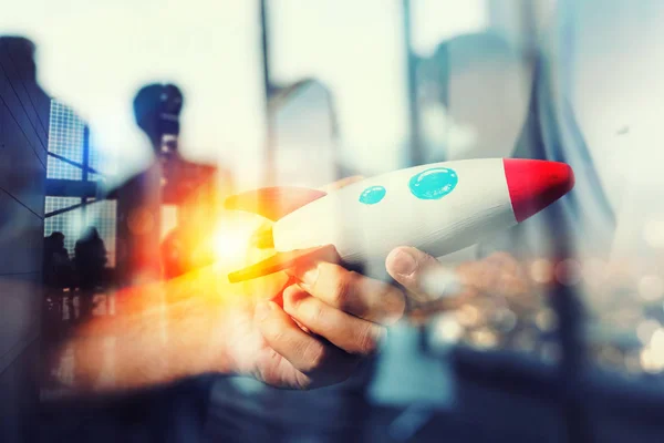 Geschäftsmann gründet sein Start-up-Unternehmen. Hand hält eine hölzerne Rakete. Doppelbelichtung mit Lichteffekten — Stockfoto