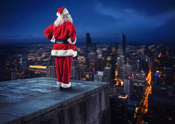 Santa Claus mira hacia abajo en la ciudad esperando para entregar los regalos —  Fotos de Stock