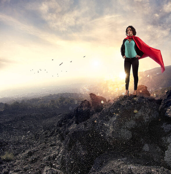 Successful businesswoman acts like a super hero on a mountain. Concept of determination and success