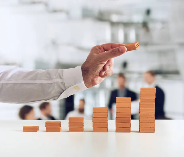 Geschäftsmann legt einen Ziegelstein auf einen Ziegelhaufen. Konzept wachsender Statistiken und Erfolge — Stockfoto