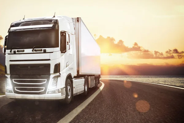 Biała ciężarówka porusza się po drodze w naturalnym krajobrazie o zachodzie słońca — Zdjęcie stockowe