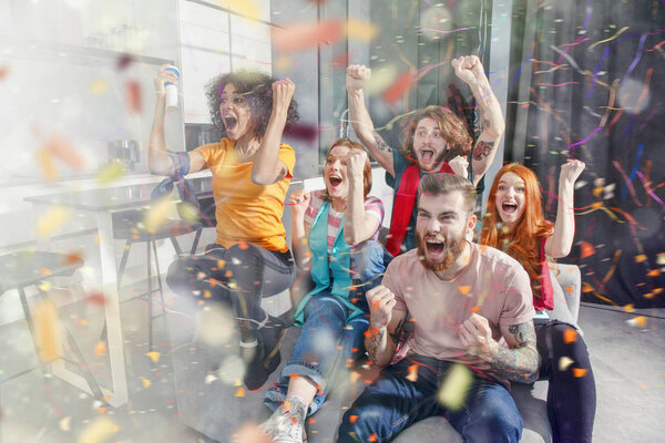 Happy friends of football fans watching soccer on tv and celebrating victory with falling confetti