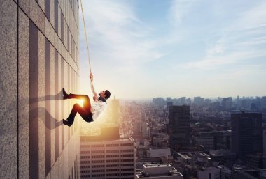 Businessman climbs a building with a rope. Concept of determination clipart