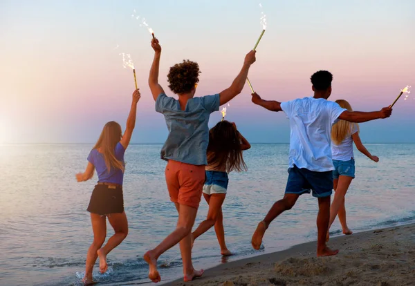 Felices amigos sonrientes corriendo por la playa con velas brillantes — Foto de Stock