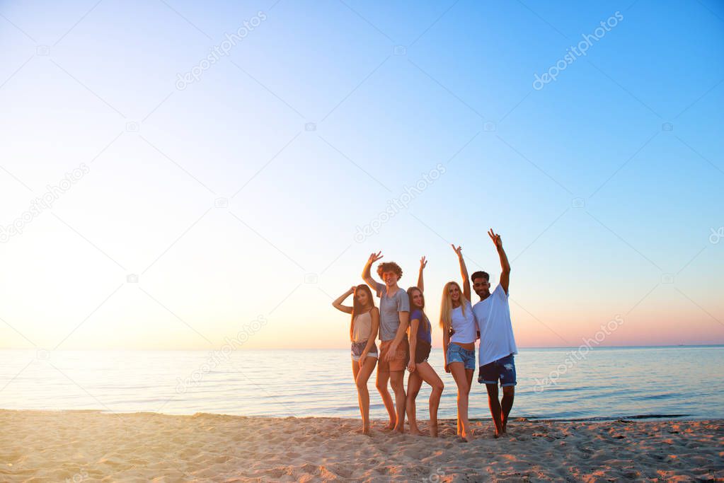 Group of happy friends having fun at ocean beach at dawn