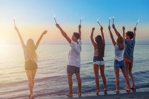 Boldog mosolygó barátok rohangálnak a parton szikrázó gyertyákkal — Stock Fotó