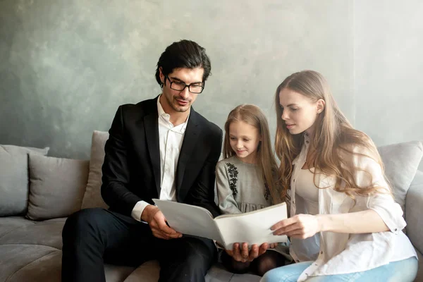 Happy little girl reads a book with her parents