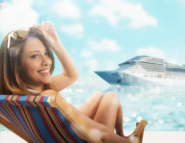 Hermosa chica sentada en una silla de cubierta en la playa al atardecer con crucero en el fondo — Foto de Stock